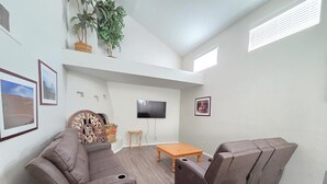 Een woonkamer met een hoekbank, een houten salontafel en een flatscreen televisie die aan de muur is bevestigd.