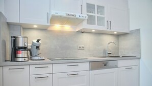 Une cuisine moderne avec des meubles blancs, une machine à café, un grille-pain et un lave-vaisselle.
