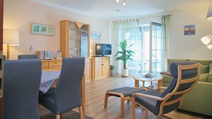 Un salon moderne avec un meuble en bois, un téléviseur, une table à manger avec des chaises, un canapé vert et une plante en pot.