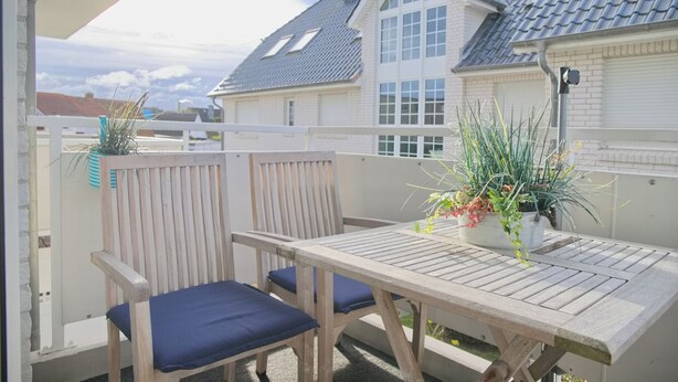 Une table et des chaises en bois sur un balcon, avec vue sur une maison.