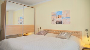 Une chambre à coucher avec un lit, une tête de lit en bois, une table de chevet avec une lampe, un miroir et un mur orné d’œuvres d’art abstraites.