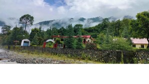 A rural setting with a stone wall, a small building with a red roof, and a sign that reads "Hotel." - Anand-Ganga Yoga Guesthouse (Bhatwari)
