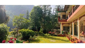 A hotel with a garden, a balcony with a railing, and a view of a mountainous area. - Anand-Ganga Yoga Guesthouse (Bhatwari)