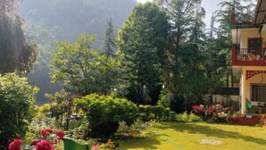 A hotel with a garden, a balcony with a railing, and a view of a mountainous area. - Anand-Ganga Yoga Guesthouse (Bhatwari)