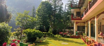 A hotel with a garden, a balcony with a railing, and a view of a mountainous area.