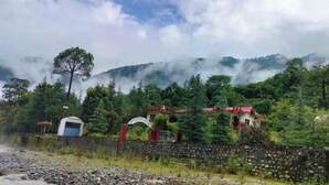 A rural setting with a stone wall, a small building with a red roof, and a sign that reads "Hotel." - Anand-Ganga Yoga Guesthouse (Bhatwari)