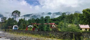 A rural setting with a stone wall, a small building with a red roof, and a sign that reads "Hotel." - Anand-Ganga Yoga Guesthouse (Bhatwari)