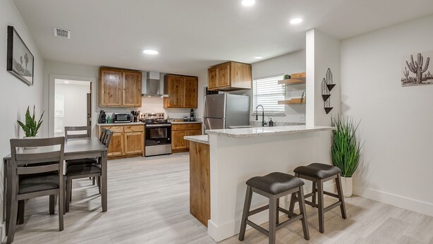 A modern kitchen with wooden cabinets, a central island, bar stools, and a dining table.