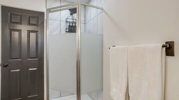 A bathroom with a glass-enclosed shower, a white towel hanging on a wall-mounted towel rack, and a dark wooden door.