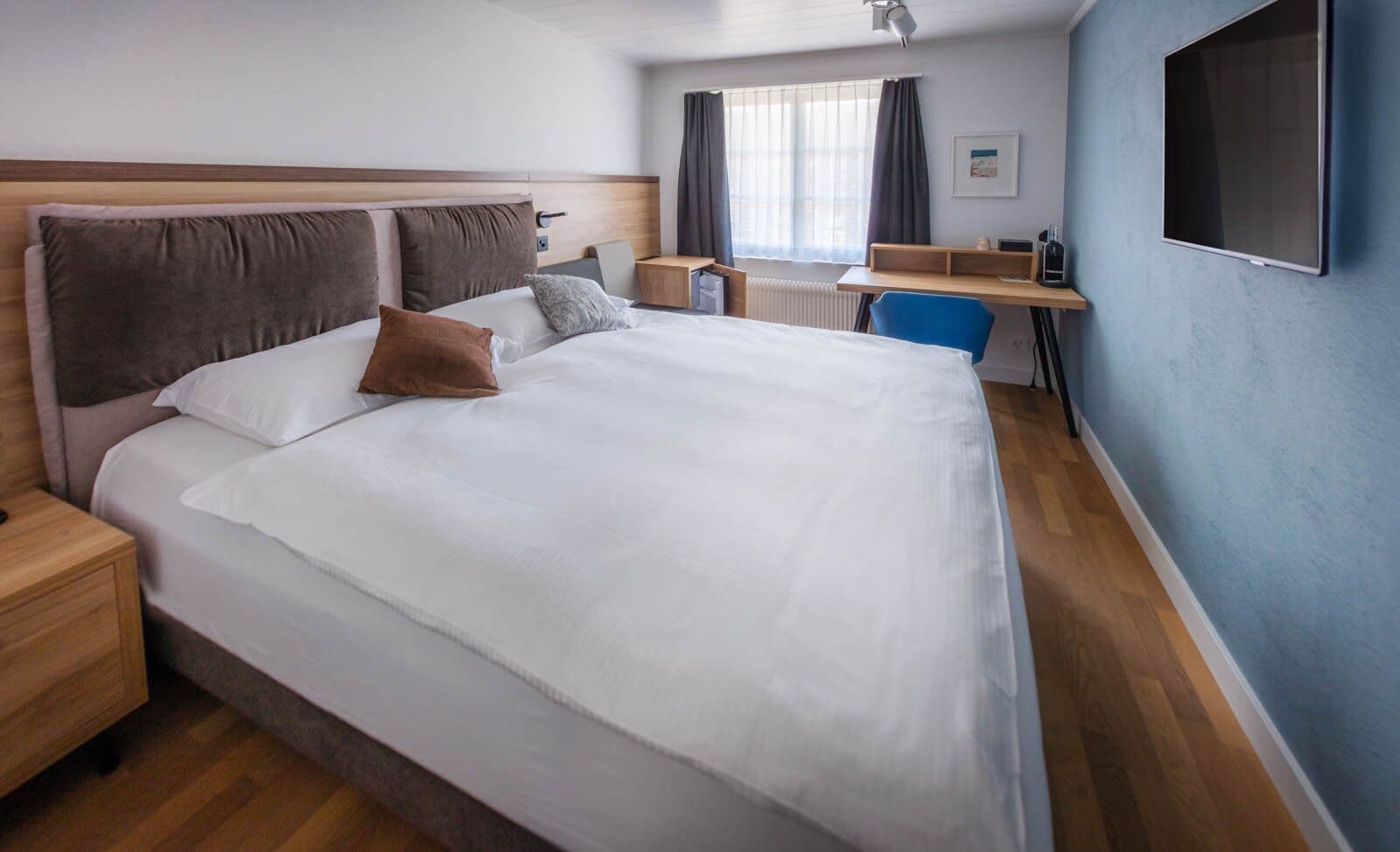 Una habitació d'hotel amb un llit gran, un escriptori, una cadira i un televisor penjat a la paret.