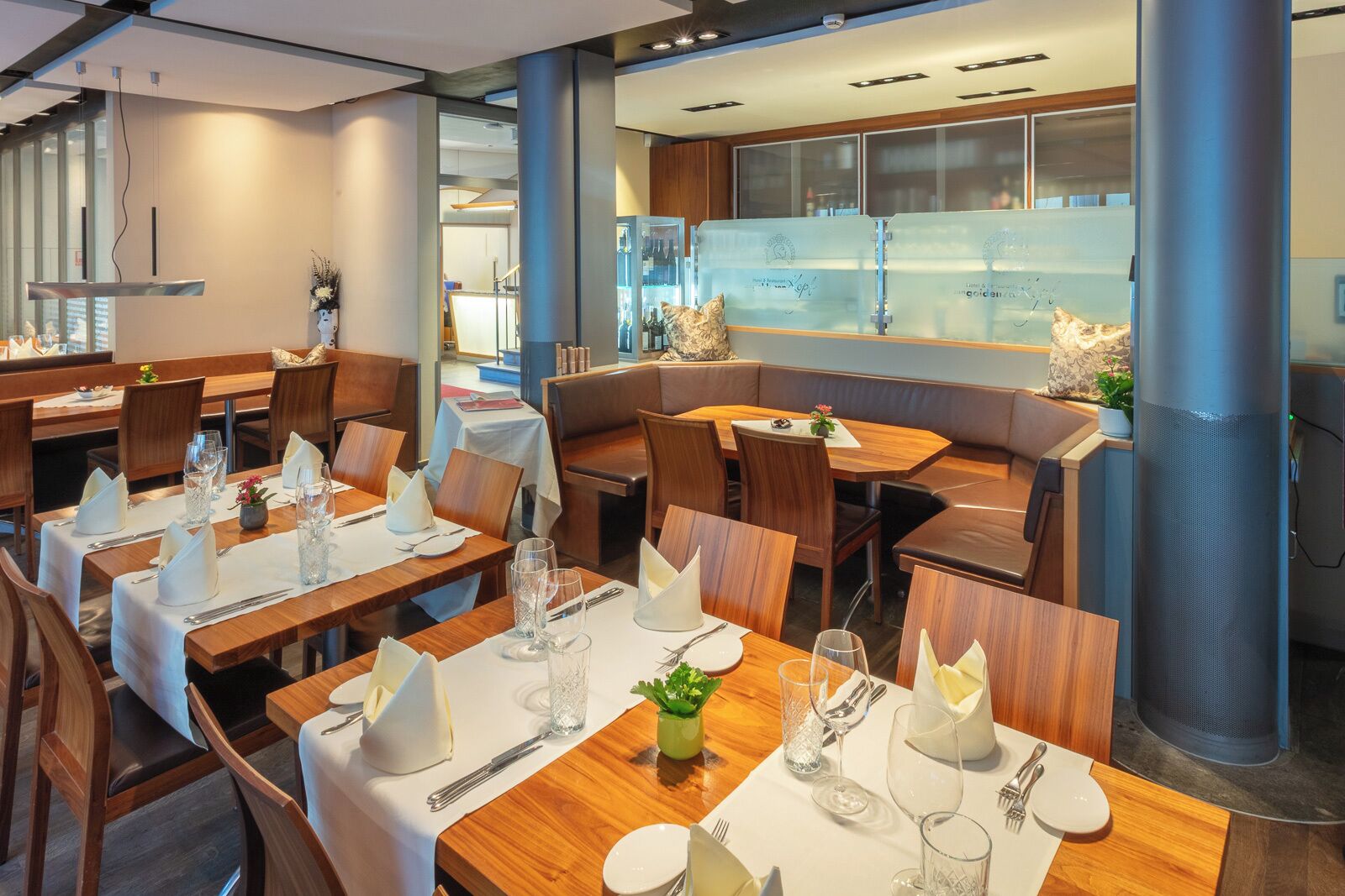 En restaurang med flera bord, vackert dukade för gästerna, med vita dukar, prydligt placerade bestick och glasvaror.