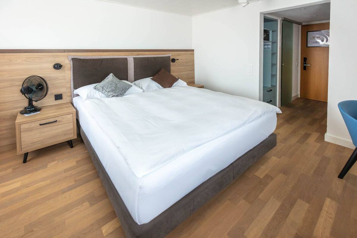 A modern bedroom with a wooden headboard, a single bed, a nightstand with a fan, and a blue chair.