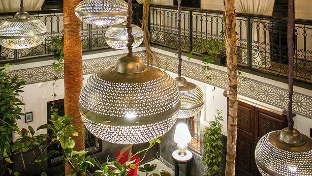 Ein Innenhof mit hängenden dekorativen Lampen, Palmen und einem gefliesten Boden.