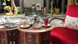Ein runder Holztisch mit Teekanne, Tassen und Snacks in einem Innenhof mit Pflanzen und einem Pool.
