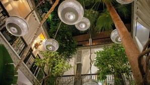Ein Innenhof mit hängenden, kugelförmigen Leuchten, Palmen und einem Balkon mit schmiedeeisernen Geländern.