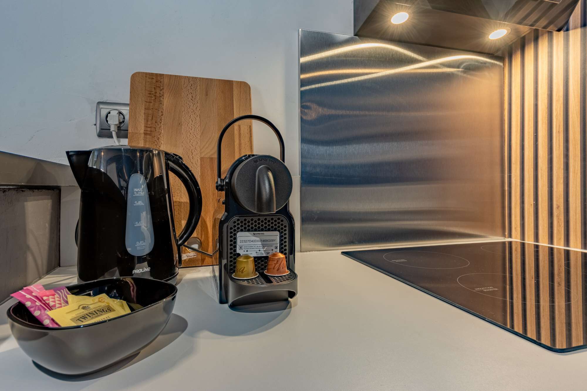 A modern kitchen with a coffee machine, a kettle, and a bowl of Twinings tea bags.