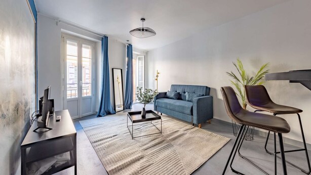 En moderne stue med sofa, sofabord, fjernsyn og en bar med barstole.