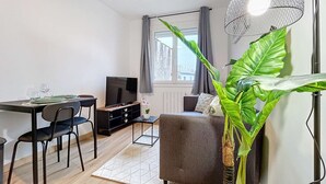 A modern living room with a dining area, a sofa, a TV, and a large plant. - [Solstice] Street Art - Duplex - Hypercentre (Pamiers)