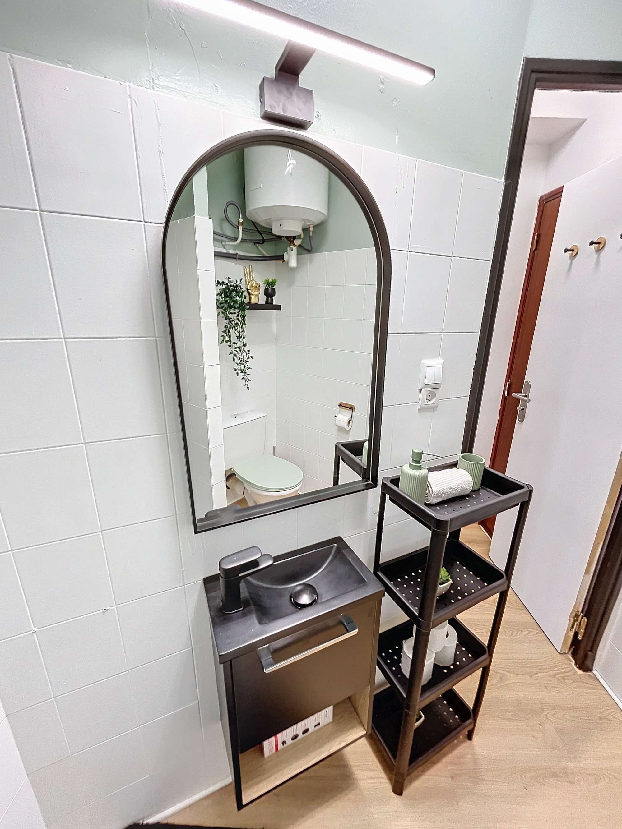 A bathroom with a large mirror, a sink, and a shelf with toiletries.