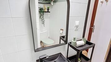 A bathroom with a large mirror, a sink, and a shelf with toiletries.