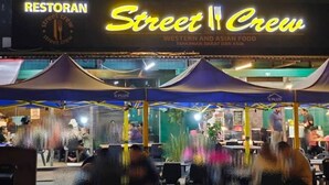 An outdoor dining area with tables and chairs under a marquee, with a sign for 'Street Crew' restaurant in the background. - Indahpura Kulai (Kulai)