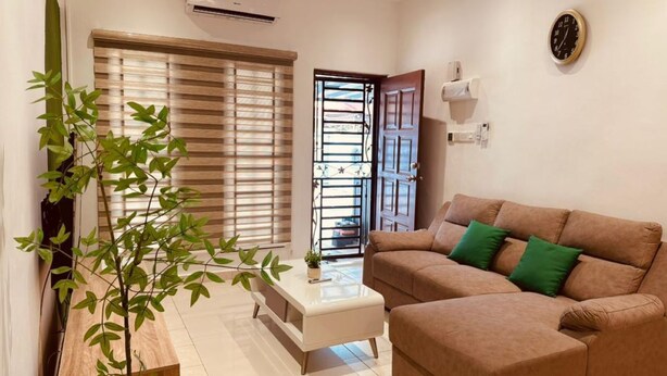 A living room with a sofa, a coffee table, a plant, and a window with blinds. - Indahpura Kulai (Kulai)