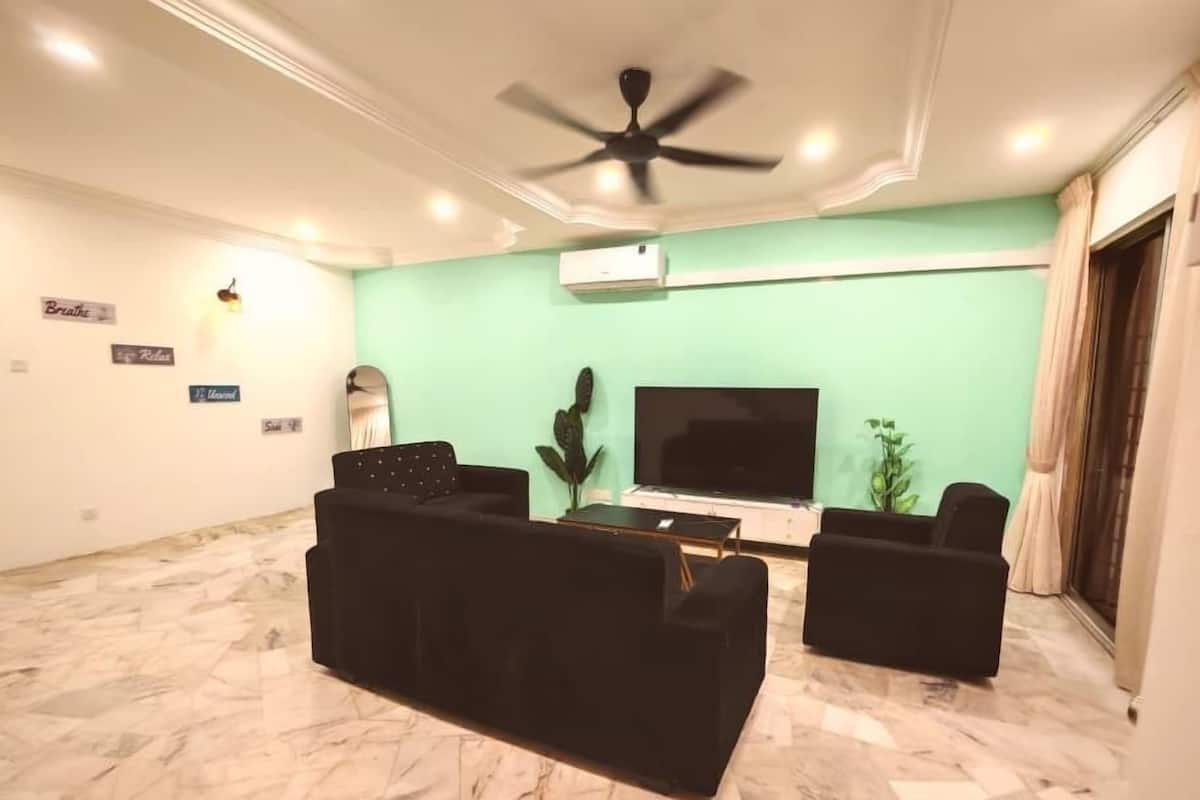 Een woonkamer met een plafondventilator, een flatscreen televisie, twee zwarte banken, een salontafel en een cactussplant.