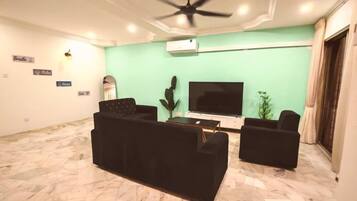 A living room with a ceiling fan, a flat-screen TV, two black sofas, a coffee table, and a cactus plant.