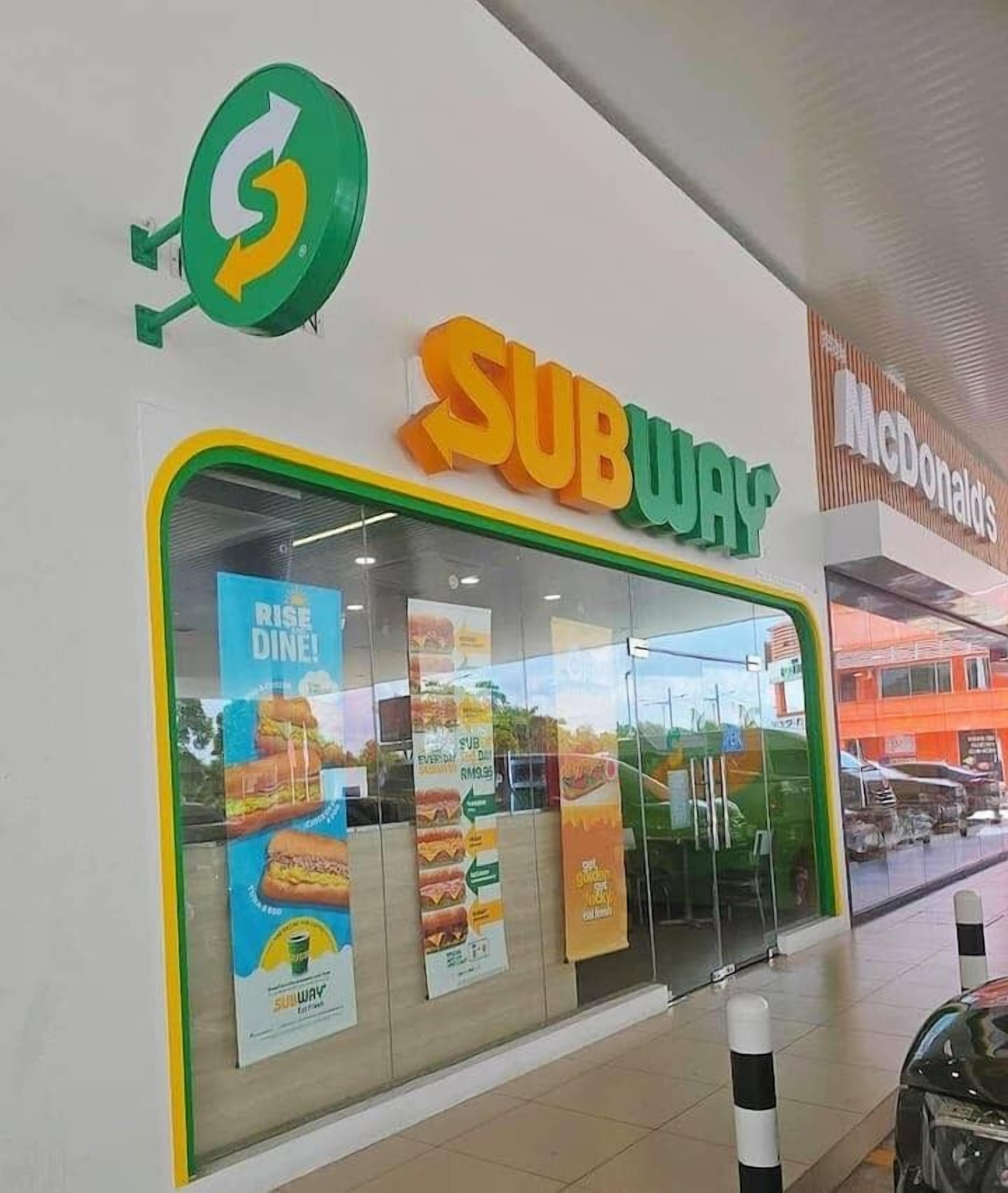 A SUBWAY restaurant with a green logo, a McDonald's sign, and promotional posters on the window.