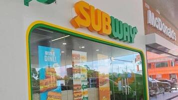 A SUBWAY restaurant with a green logo, a McDonald's sign, and promotional posters on the window.