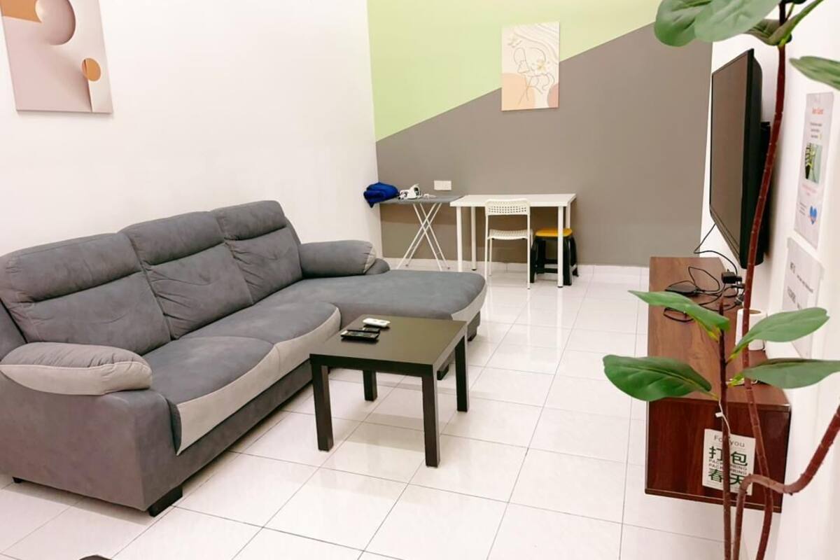 Een woonkamer met een grijze bank, een kleine tafel, een televisie en een plant.