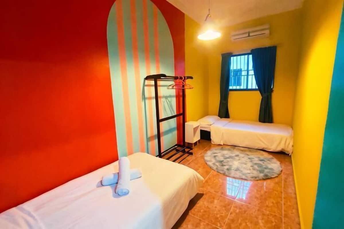 Een kamer met twee bedden, een klein rond tapijt, een raam met gordijnen en een wandrek.