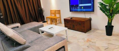 A living room with a sofa, a television, a wooden cabinet, a potted plant, and a fan.