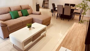 A modern living room with a sofa, a coffee table, and a dining area with chairs and a table. - Indahpura Kulai (Kulai)