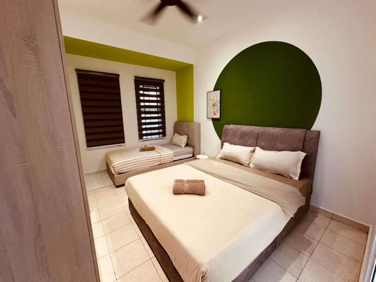 Une chambre avec un lit, un canapé-lit, un mur d’accent de couleur verte et un ventilateur de plafond.