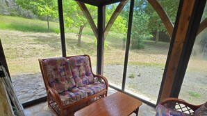Un patio cubierto con mobiliario de mimbre, suelo de piedra y amplias ventanas que dan a una zona verde.