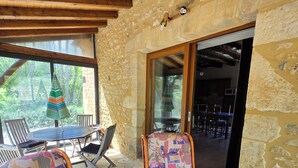 Un espacio al aire libre cubierto con sillas de mimbre y una mesa, paredes de piedra y vistas al jardín.