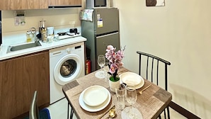 Cocina compacta con armarios de madera, lavadora, microondas y refrigerador. Hay una mesa de comedor puesta con platos, vasos y cubiertos.
