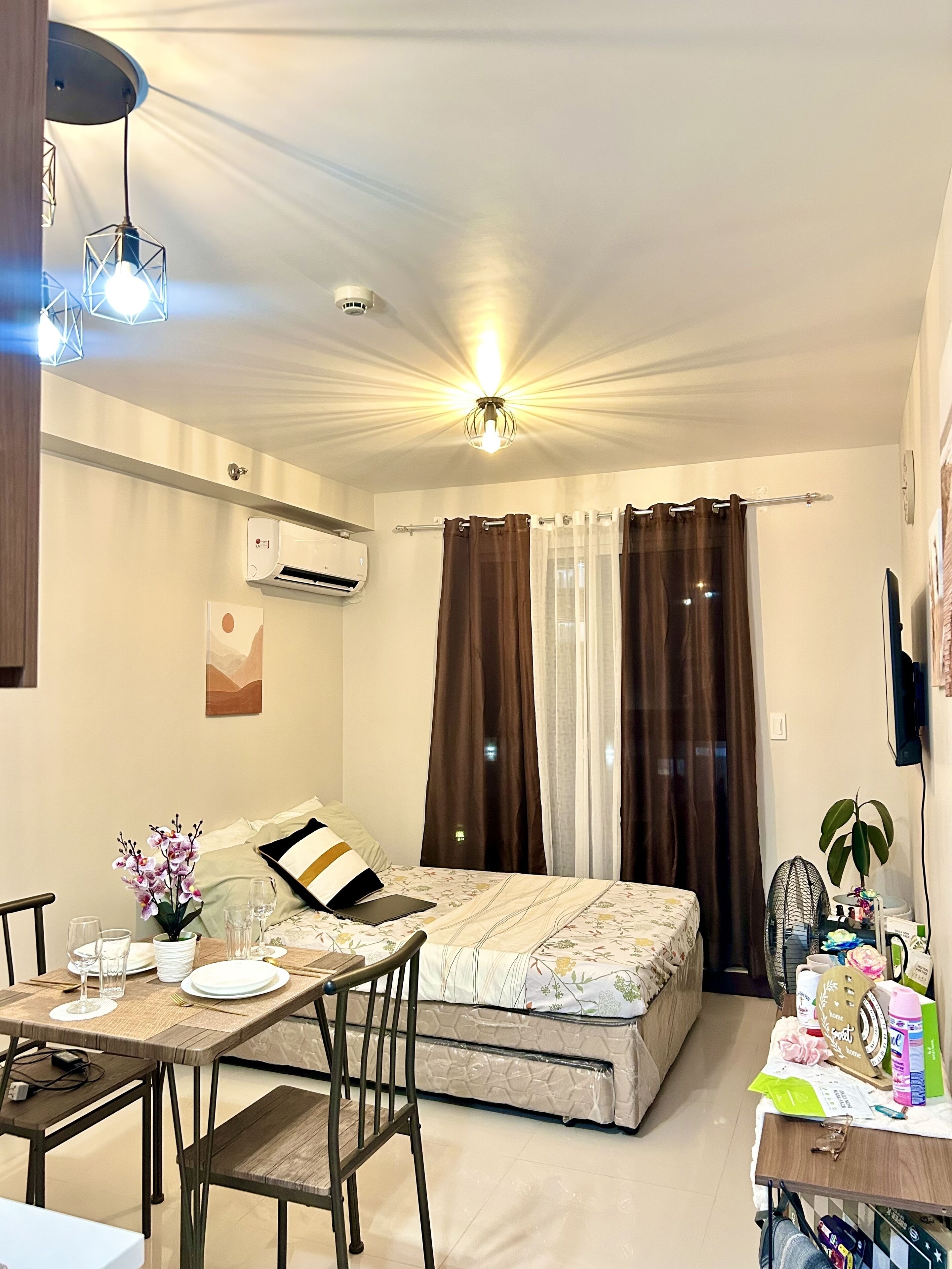 Un espacio habitable compacto con cama, una mesa de comedor con sillas, una pequeña zona de kitchenette y una lámpara de techo.
