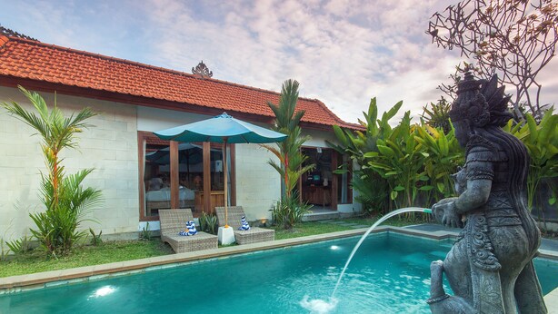A swimming pool with a statue, a house with a red roof, and a patio with lounge chairs. - Tranquil Maha Villa Ubud (Ubud)