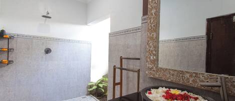A bathroom with a large mirror, a black basin with flowers, and a shower area.