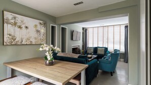 A living room with a wooden dining table, teal sofas, and a large abstract painting on the wall.