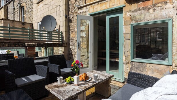 An outdoor seating area with wicker furniture, a stone table with breakfast items, and a stone building with a door and window.