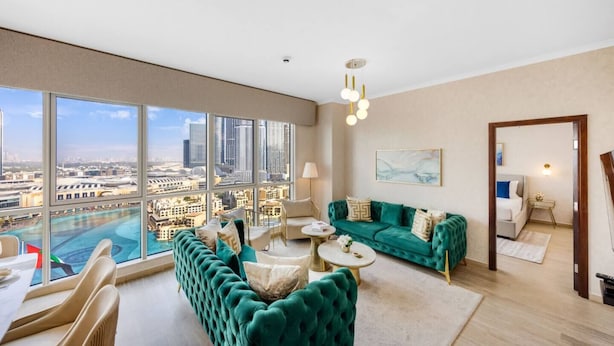 Ein geräumiges Wohnzimmer mit großem Fenster und Blick auf die Stadt, ausgestattet mit einem grünen Sofagarnitur, einem Couchtisch und einer modernen Kronleuchter.