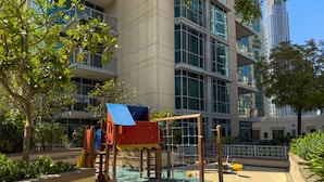 Ein Spielplatz mit Klettergerüsten und einer Rutsche, umgeben von einem Gebäude mit großen Fenstern und modernem Design.