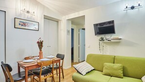 A dining area with a wooden table set for four, a green sofa, and a flat-screen TV mounted on the wall. - Charming Duplex Le Marais/beaubourg (Paris)