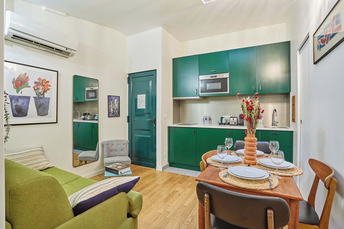 Un espacio habitable compacto con comedor, kitchenette y un sofá verde.