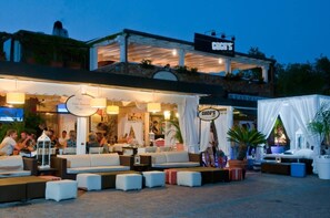 Un espace extérieur aménagé avec des canapés et des tables confortables, une terrasse couverte et une enseigne indiquant « CUGU’S ».