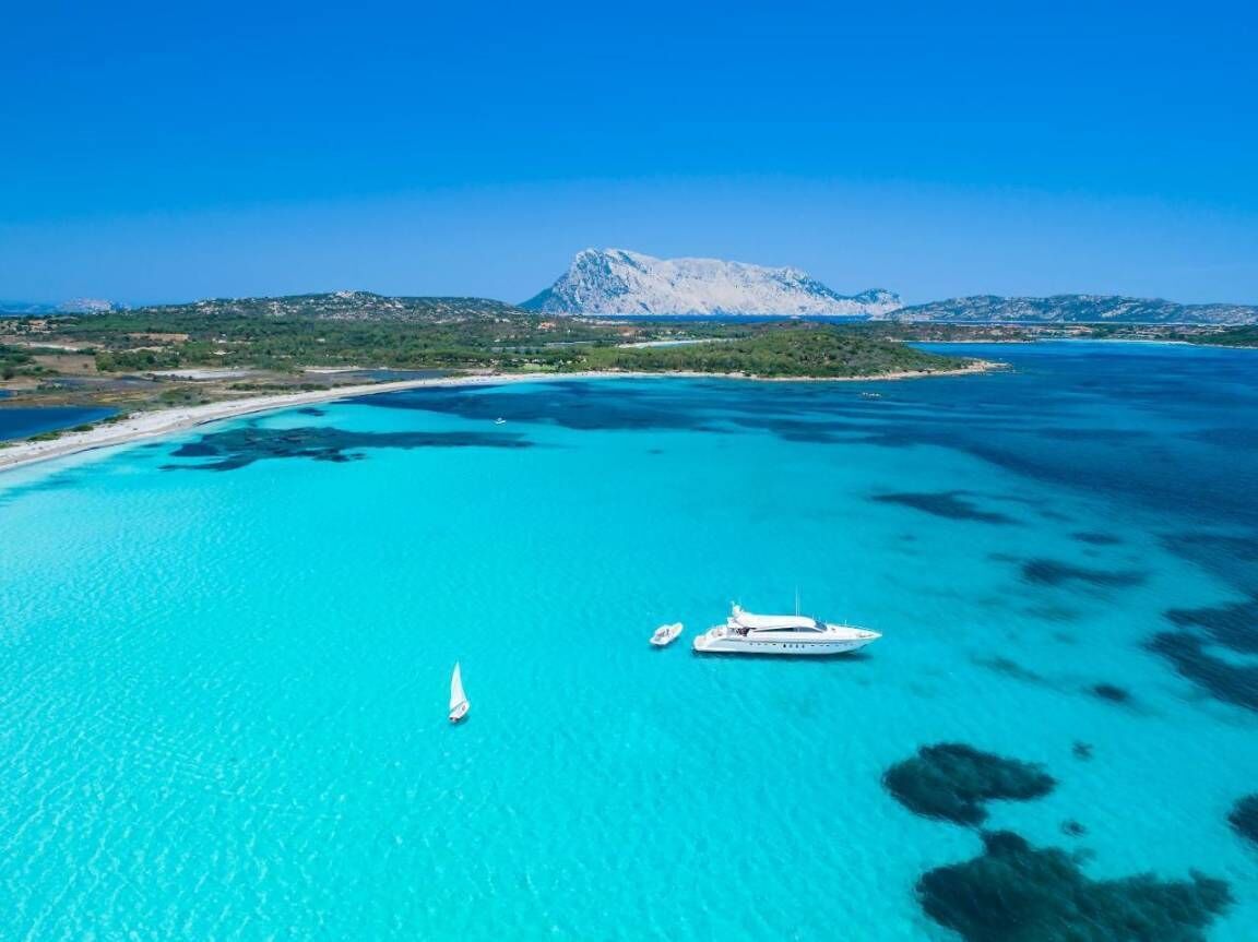 A coastal area with clear turquoise waters, a yacht, and a sailboat.