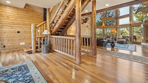 Un interior espacioso con una escalera de madera, ventanas amplias y una zona de estar acogedora.
